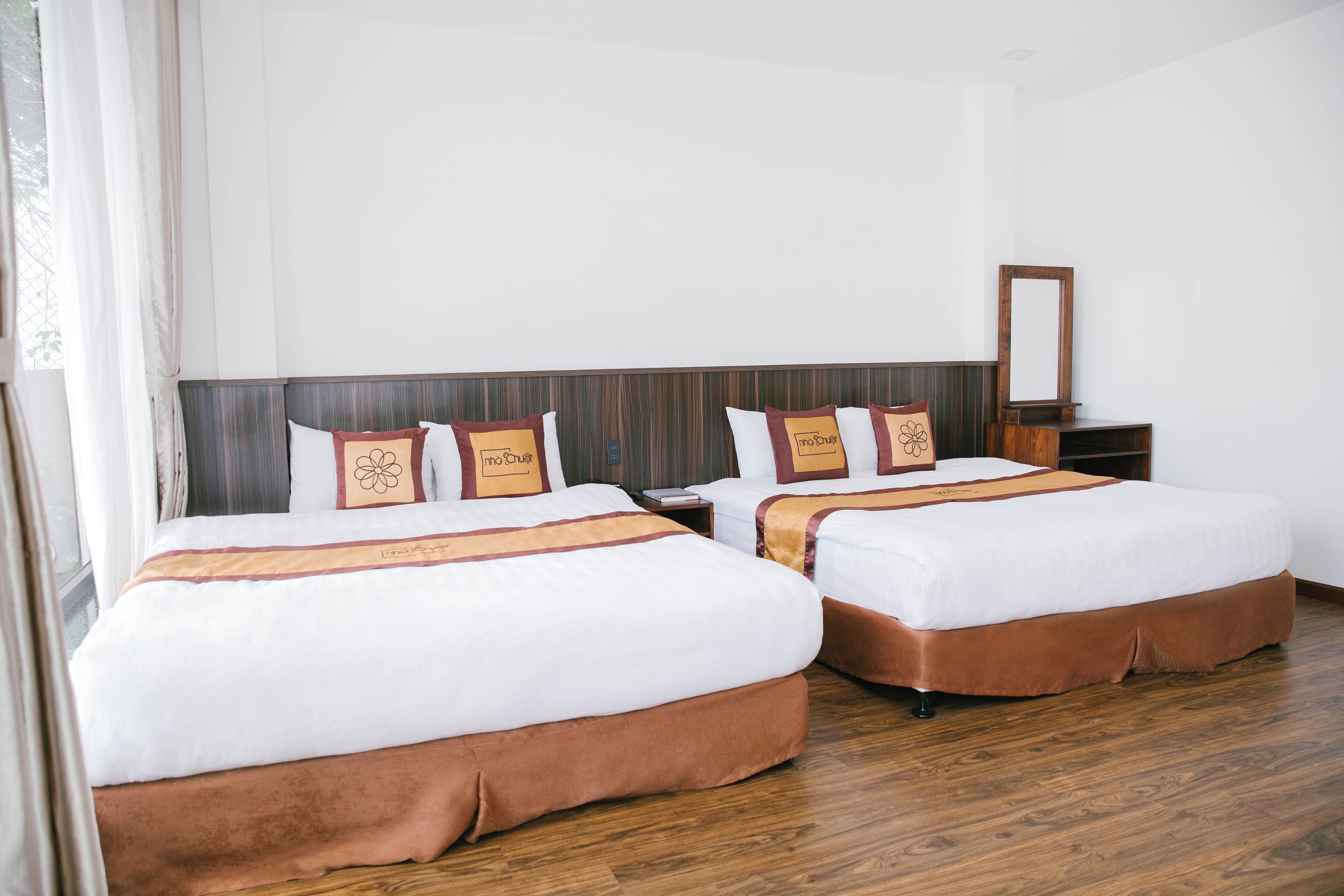 Une chambre d’hôtel avec deux lits, un plancher en bois et une table de chevet avec un miroir.