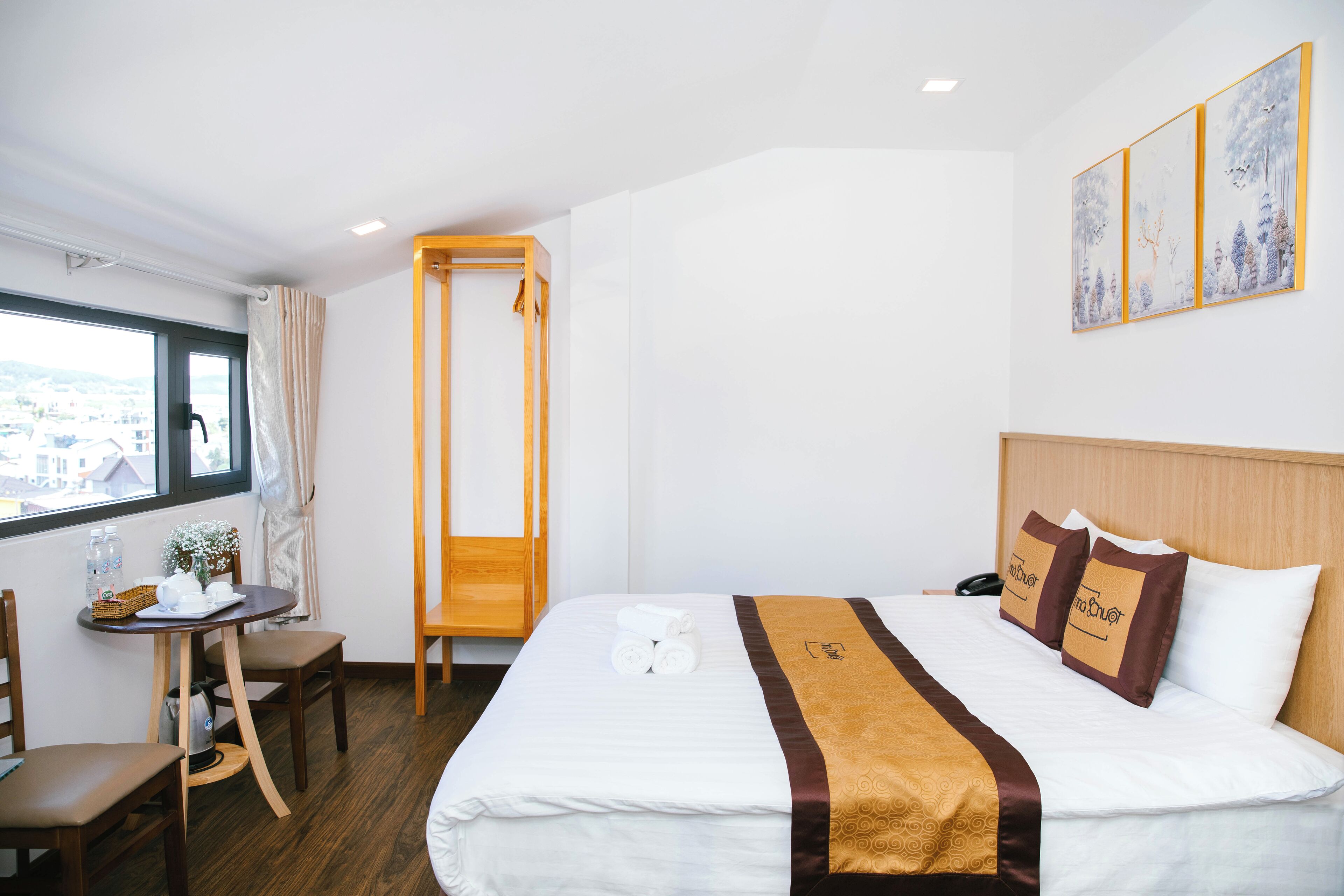 Una habitación de hotel con una cama, una mesita con una silla, una ventana y un cuadro en la pared.