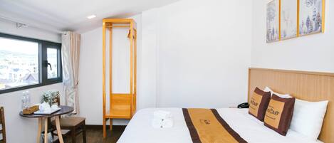 Una habitación de hotel con una cama, una mesita con una silla, una ventana y un cuadro en la pared.