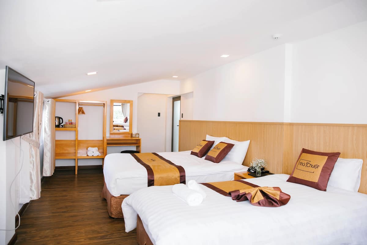 Ett hotellrum med två sängar, trägavlar, vitt sänglinne och ett trägolv.