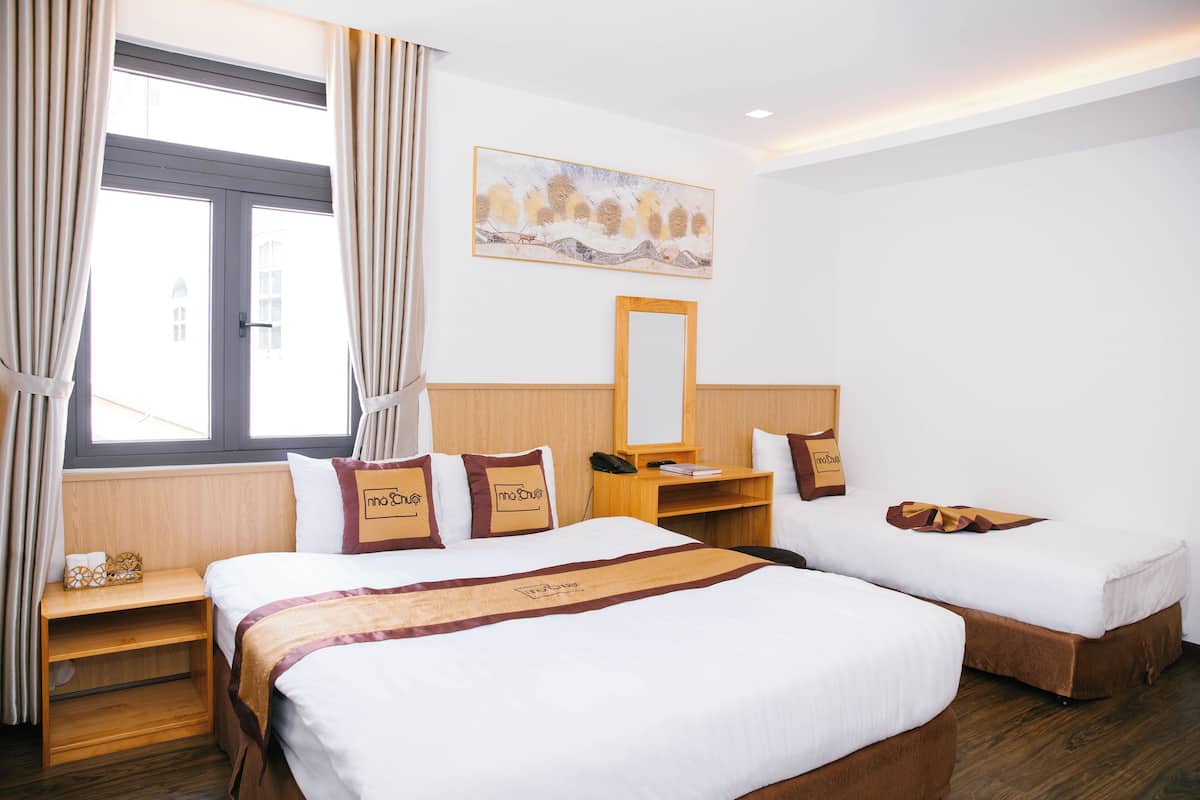 Ett hotellrum med två sängar, ett skrivbord, en stol, ett fönster med gardiner och en tavla på väggen.