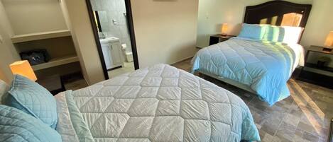 Quarto de hotel com duas camas, banheiro, televisão e uma estante com uma mala.