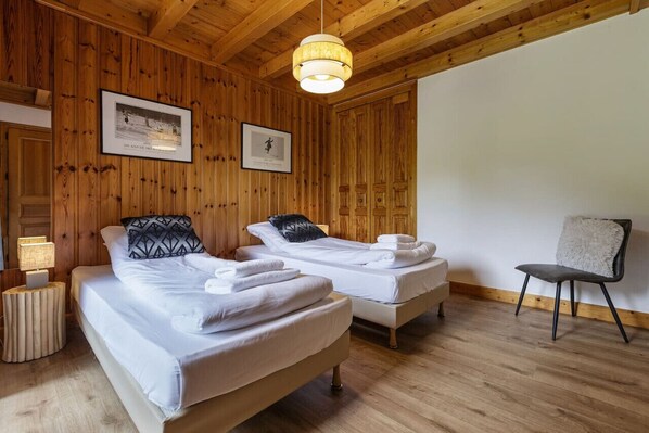 Una habitación con paneles de madera, dos camas, una silla y un lámpara colgante.