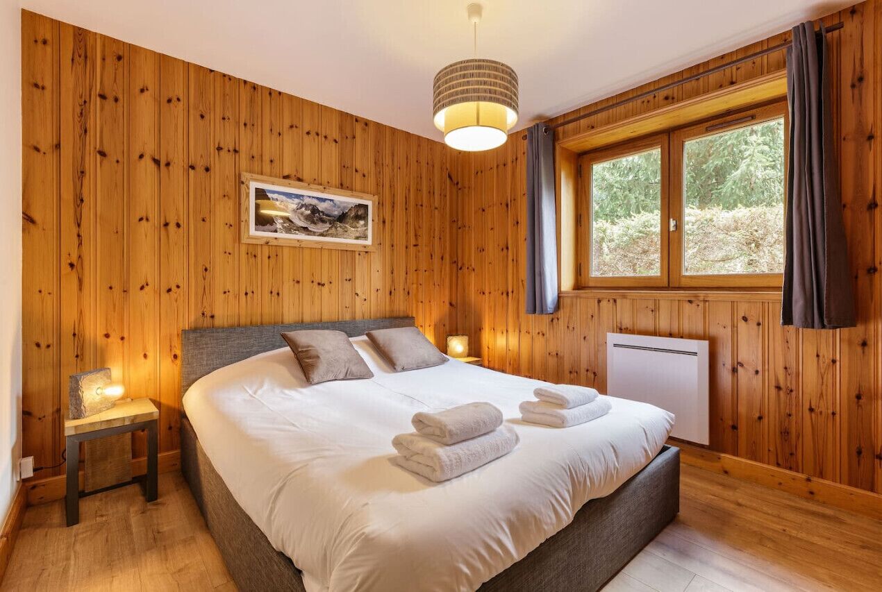 Une chambre aux murs lambrissés, avec un grand lit, un tableau accroché au mur et une fenêtre avec des rideaux.