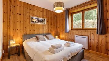 A wooden-paneled bedroom with a large bed, a picture on the wall, and a window with curtains.