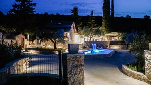 A stone-walled pool area with a fountain, surrounded by trees and a stone building. - Amazing home in Postira (Postira)