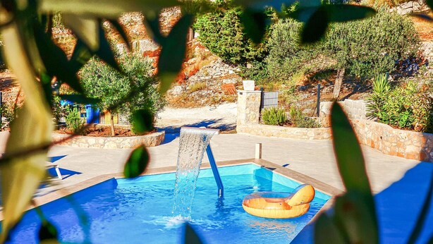 A swimming pool with a water feature, surrounded by stone walls and greenery. - Amazing home in Postira (Postira)