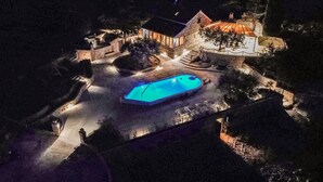 A nighttime view of a house with a swimming pool, stone walls, and a well-lit entrance. - Amazing home in Postira (Postira)