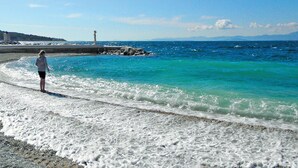 A beach with clear turquoise water, a person standing on the shore, and a lighthouse in the background. - Amazing home in Postira (Postira)