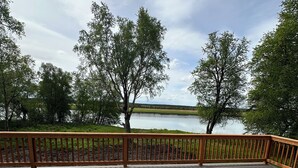Una terraza de madera con barandilla que da a un cuerpo de agua y árboles.