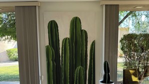 A spacious room with a large cactus wall art, a potted plant, and a modern chair.
