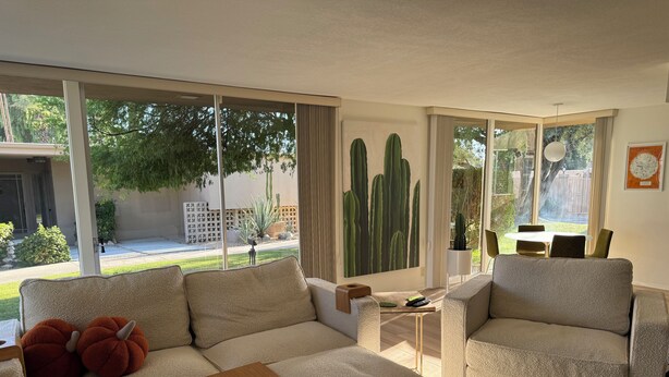 A modern living room with a beige sofa, a wooden coffee table, and a view of a garden through large windows.