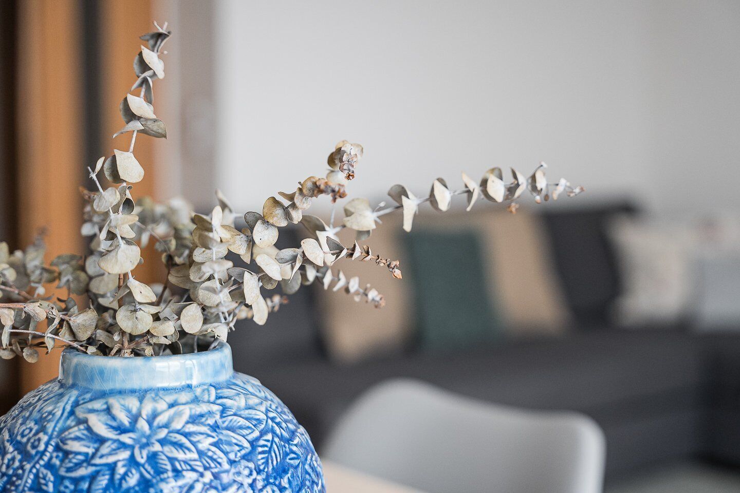A blue vase with a floral pattern containing dried eucalyptus branches.