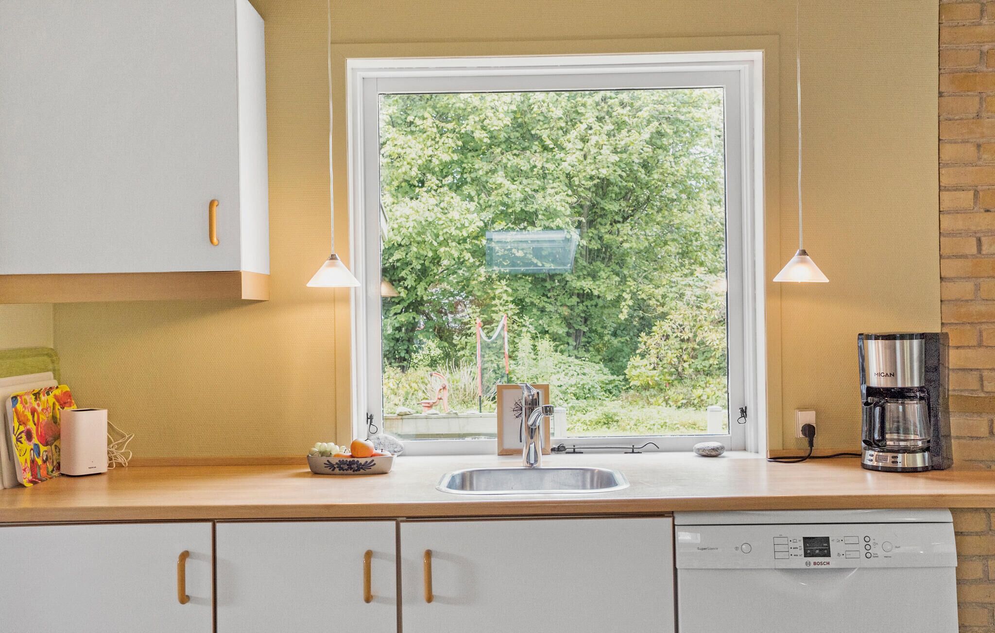 Une cuisine moderne avec des meubles blancs, un lave-vaisselle Bosch, un évier et une fenêtre donnant sur un paysage verdoyant.