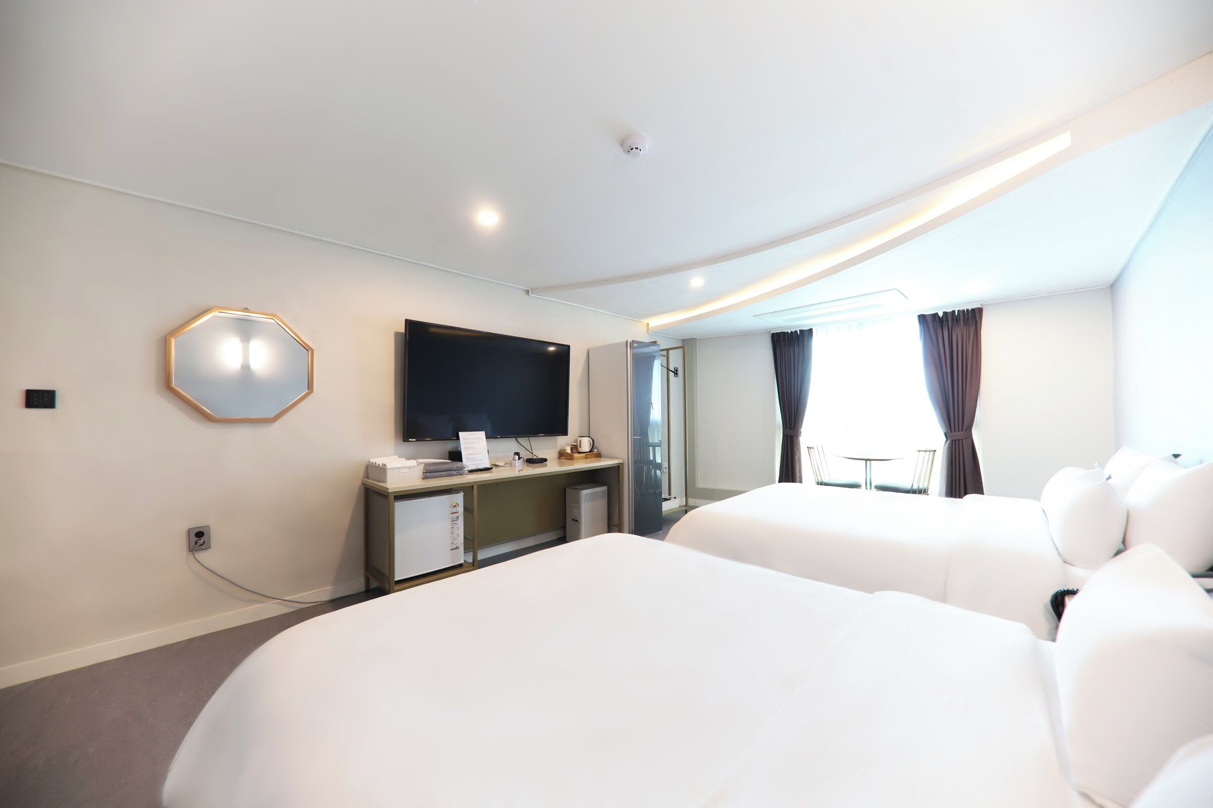 A hotel room with two beds, a flat-screen TV, a desk with a computer, and a large mirror.
