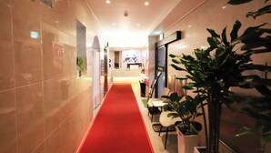 A hotel corridor with a red carpet, tiled walls, and a reception desk in the distance. - BRIGHTEN HOTEL (Jeonju)