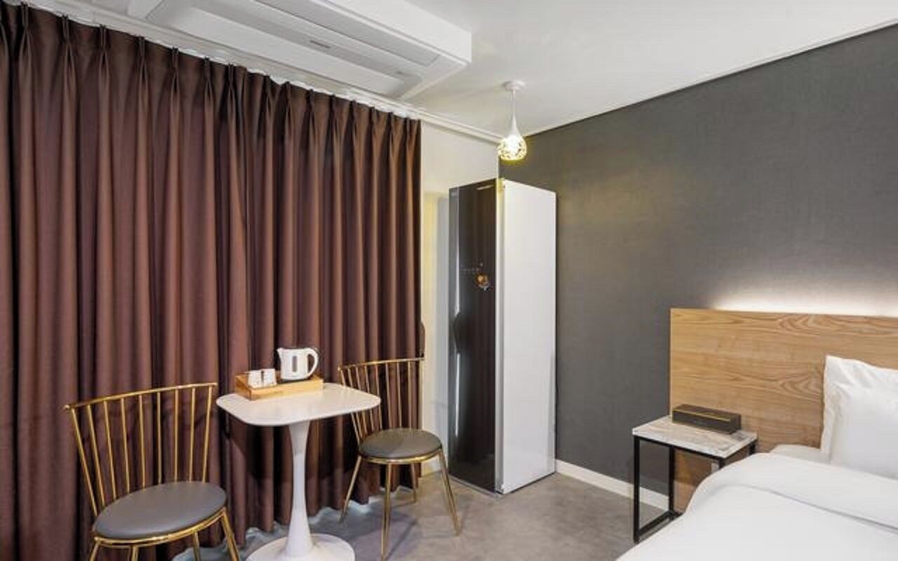 A hotel room with a bed, a small table with chairs, a nightstand, and a wardrobe.