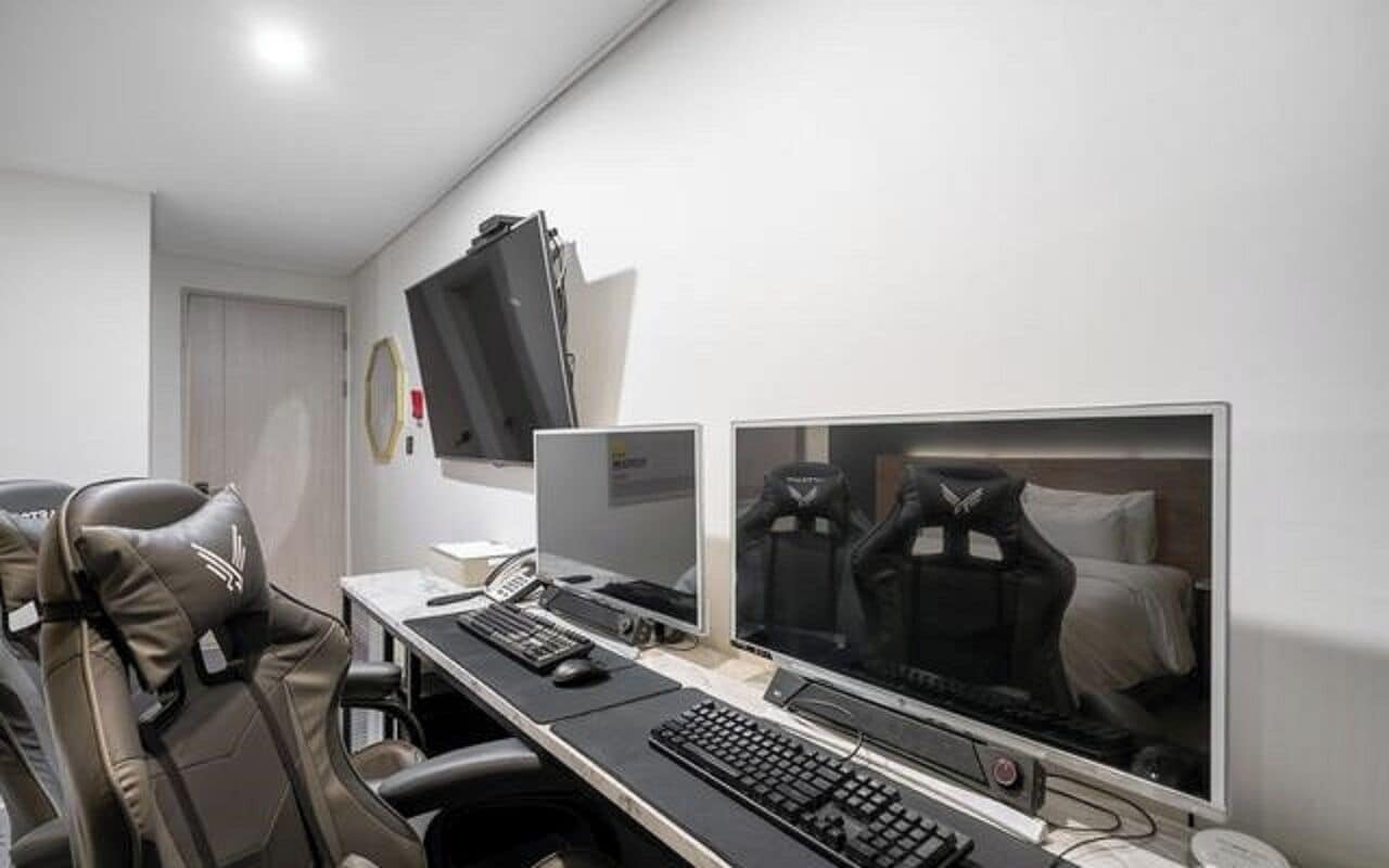 Ein Hotelzimmer mit Schreibtisch, zwei Monitoren, einer Tastatur und einem Headset.