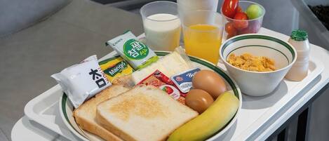 Una bandeja con alimentos para el desayuno, como tostadas, huevos, un plátano, leche, jugo de naranja y cereal.