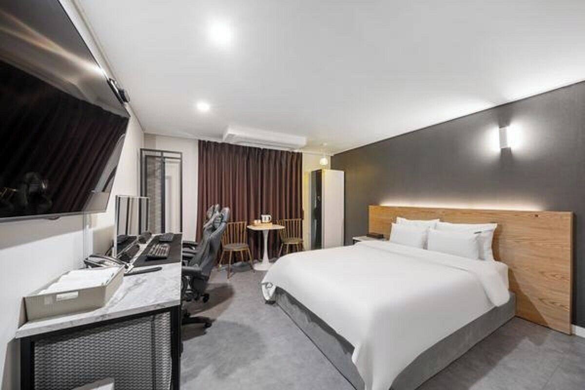A modern hotel room with a large bed, a desk with a computer, a chair, and a TV.