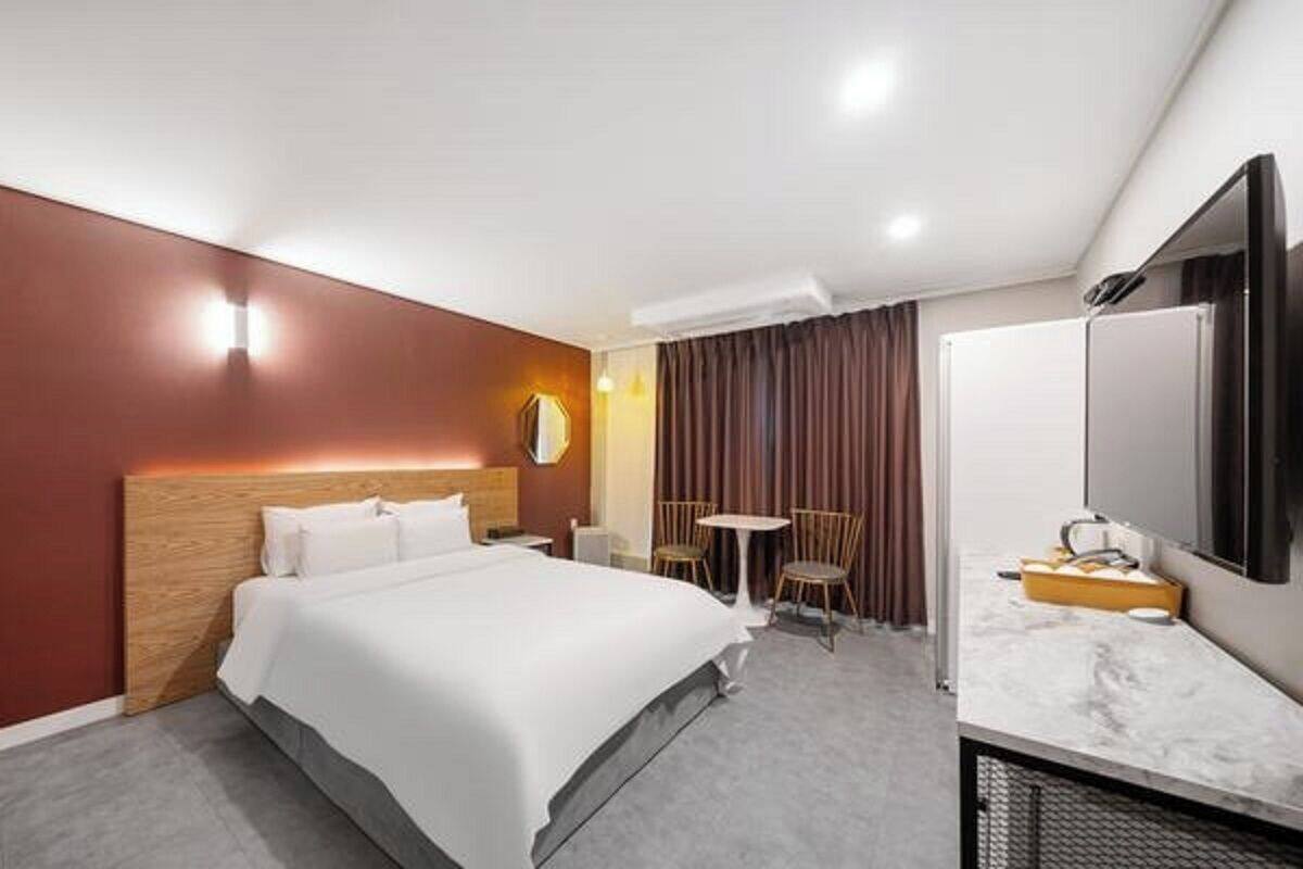 A hotel room with a bed, a desk, a chair, a TV, and a window with curtains.