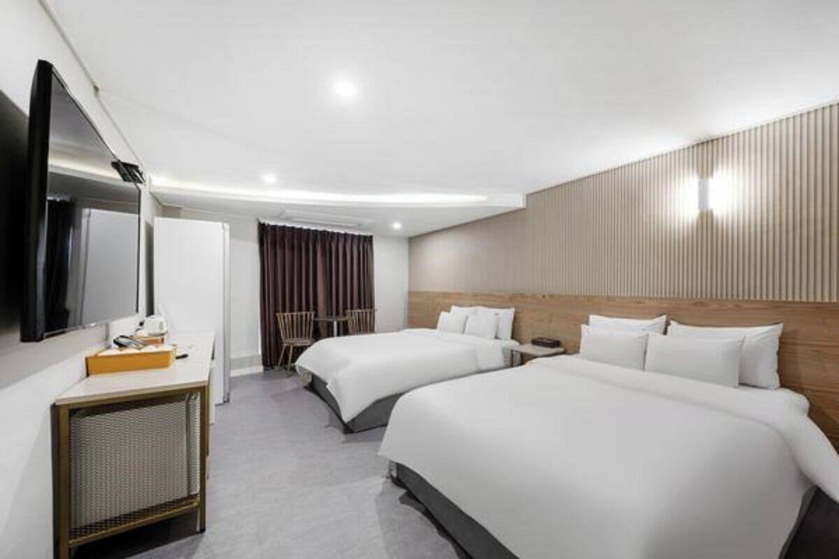 A modern hotel room with two beds, a desk, a TV, and a large mirror.