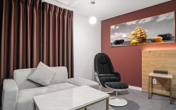 A modern room with a white sofa, a black chair, a small table, and a painting of a ship on the wall. - BRIGHTEN HOTEL (Jeonju)