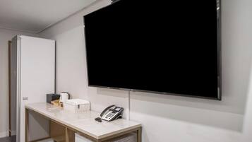 Une chambre d’hôtel dotée d’un grand téléviseur à écran plat fixé au mur, d’un bureau avec un téléphone, d’une machine à café et d’une petite boîte.