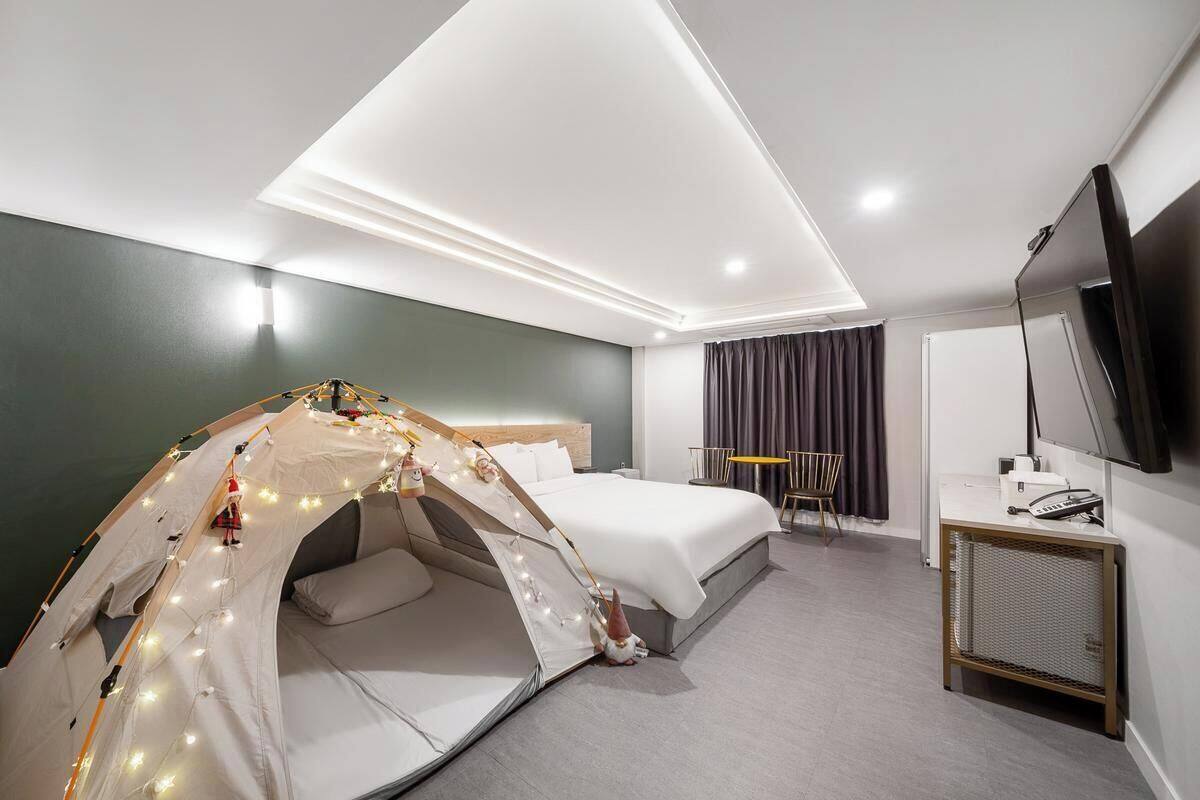 A hotel room with a bed, a small desk, a TV, and a tent-like structure with lights.