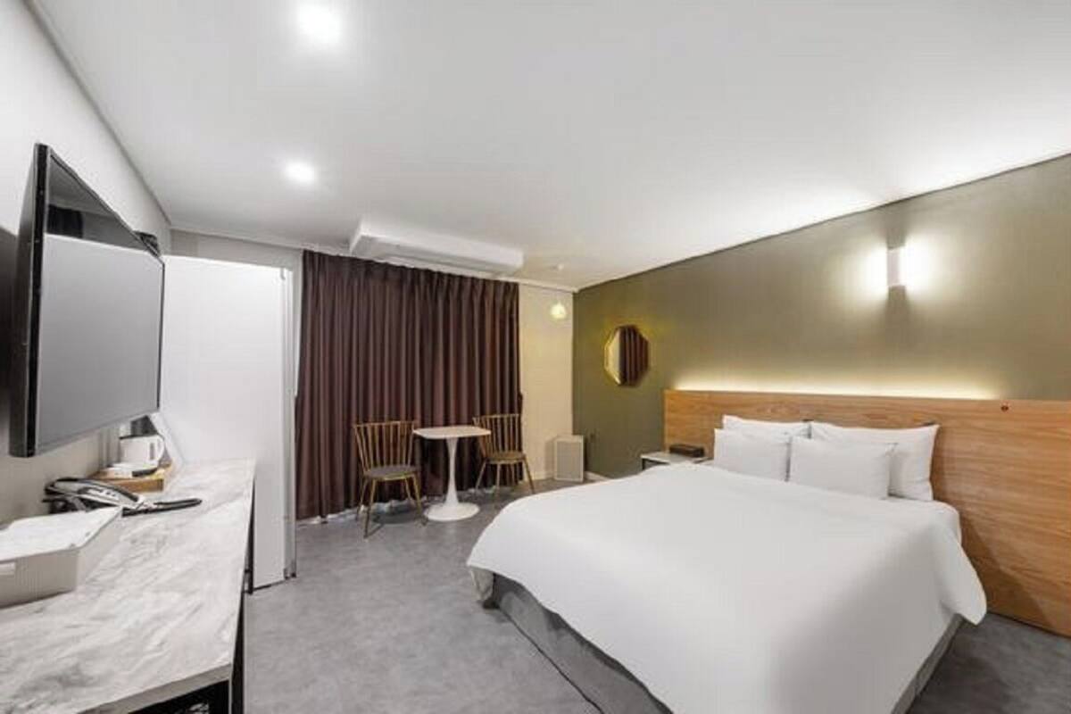 A modern hotel room with a large bed, a desk with a flat-screen TV, a small round table, and a chair.
