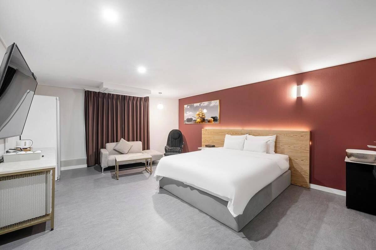 A modern hotel room with a large bed, a desk, a chair, a TV, and a wall-mounted light fixture.