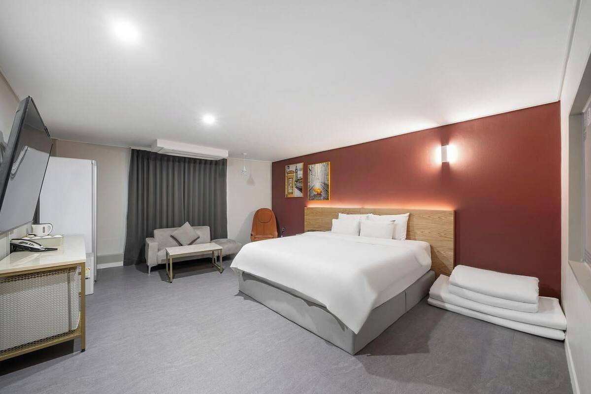 A modern hotel room with a large bed, a desk, a chair, and a sofa.