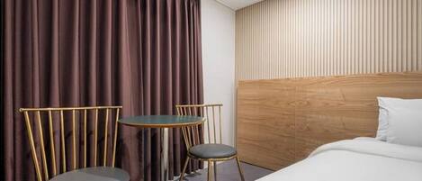 A hotel room with a bed, two chairs, a small table, and a curtain.