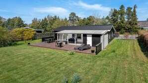 Une maison moderne dotée d’un patio, d’un barbecue et d’une pelouse bien entretenue.