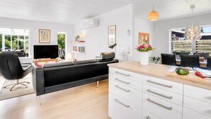 Une cuisine moderne avec des meubles blancs, un îlot central doté de tiroirs, un coin repas avec des chaises et une grande fenêtre qui laisse entrer la lumière naturelle.