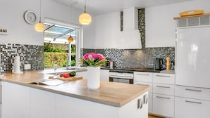Une cuisine moderne avec des meubles blancs, un plan de travail en bois, un four encastré et un pare-feu décoré de mosaïques.