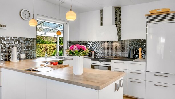 Une cuisine moderne avec des meubles blancs, un plan de travail en bois, un four encastré et un pare-feu décoré de mosaïques.