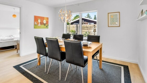 Un espace repas moderne avec une table en bois, des chaises noires et un tapis noir et gris.