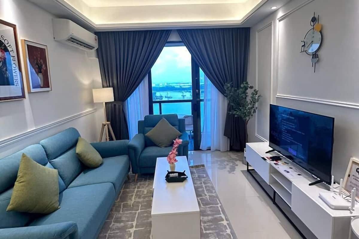A modern living room with a blue sofa, a white coffee table, a TV, and a view of the city through large windows.