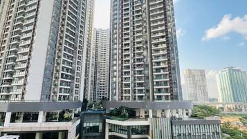 Un edificio residencial alto con varios balcones, una entrada moderna y un área ajardinada con árboles.