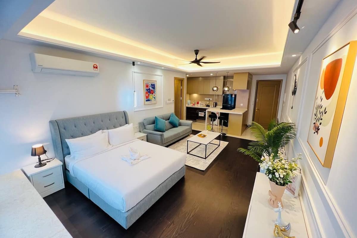 A modern hotel room with a large bed, a sofa, a coffee table, and a dining area.