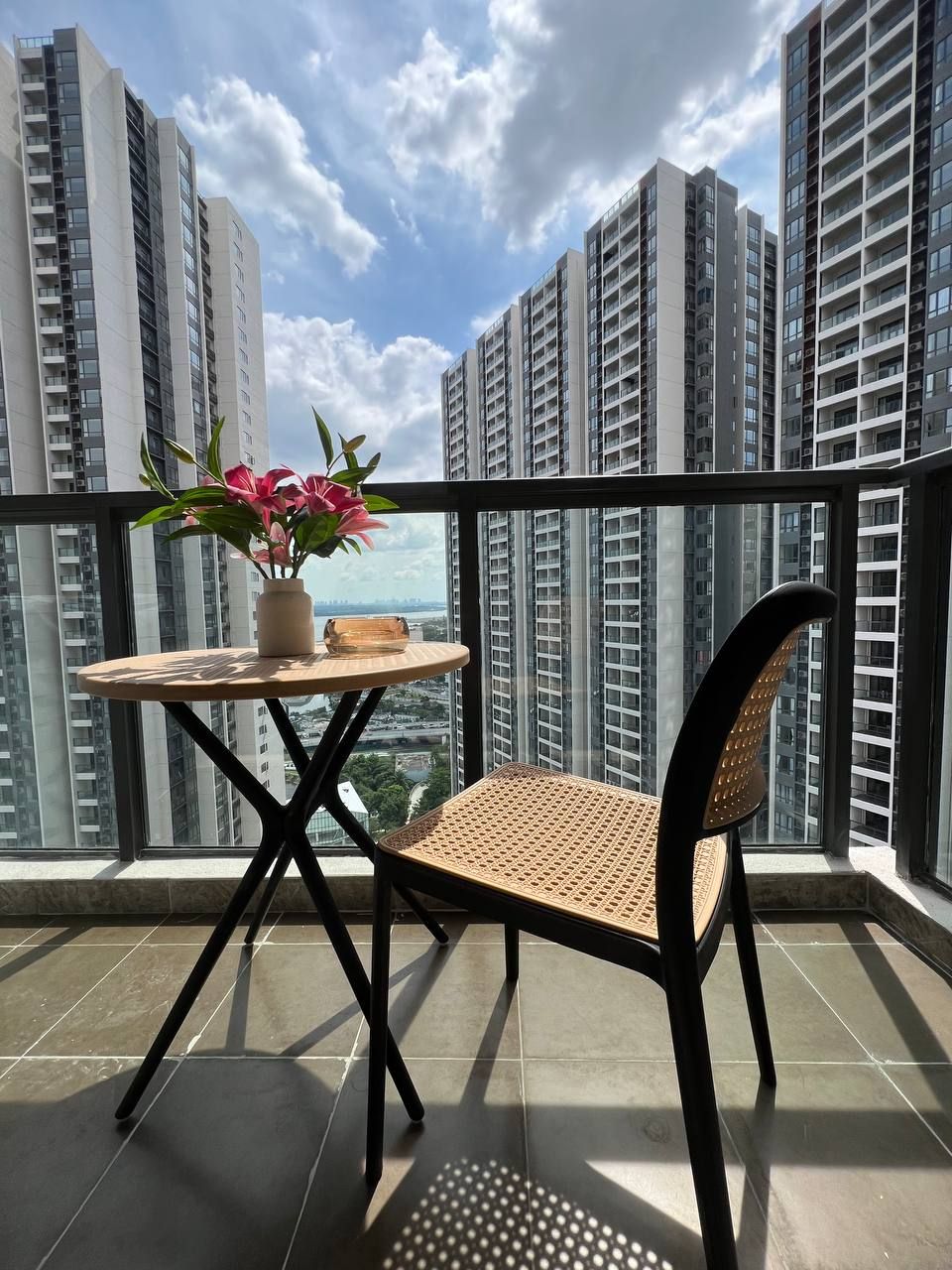Un balcón con una mesa y una silla, una planta en maceta y vistas de edificios altos.