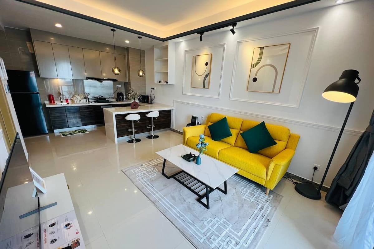 A modern living room with a yellow sofa, a white coffee table, and a kitchen in the background.