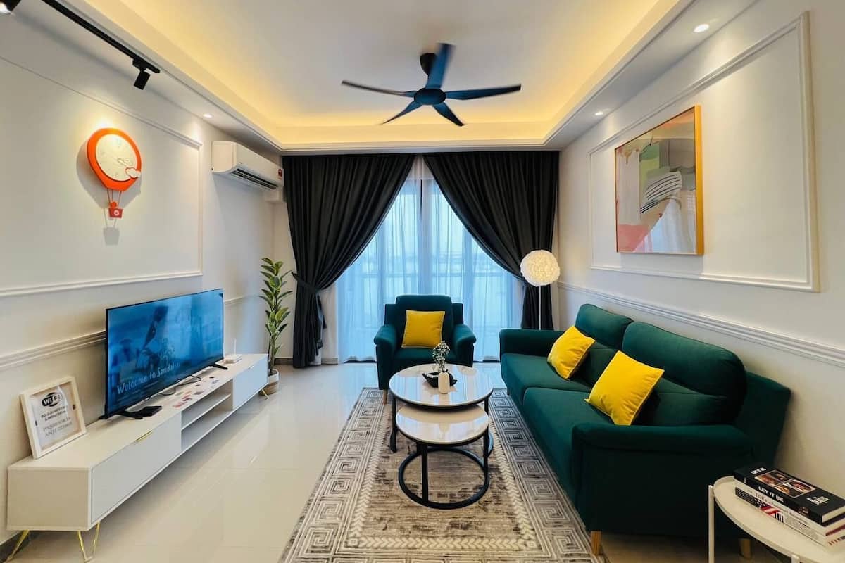 A modern living room with a flat-screen TV, a ceiling fan, a green sofa with yellow cushions, a coffee table, and a large window with curtains.