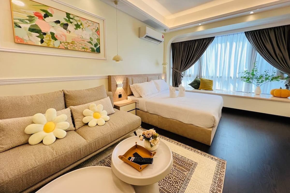 A modern hotel room with a sofa, a bed, a bedside table, and a window with curtains.