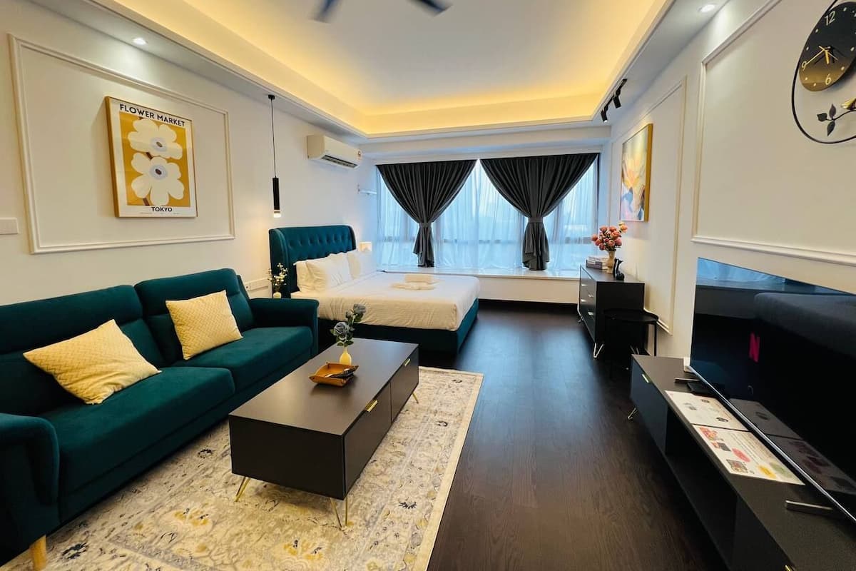 A modern hotel room with a teal sofa, a bed with dark curtains, a flat-screen TV, and a ceiling fan.