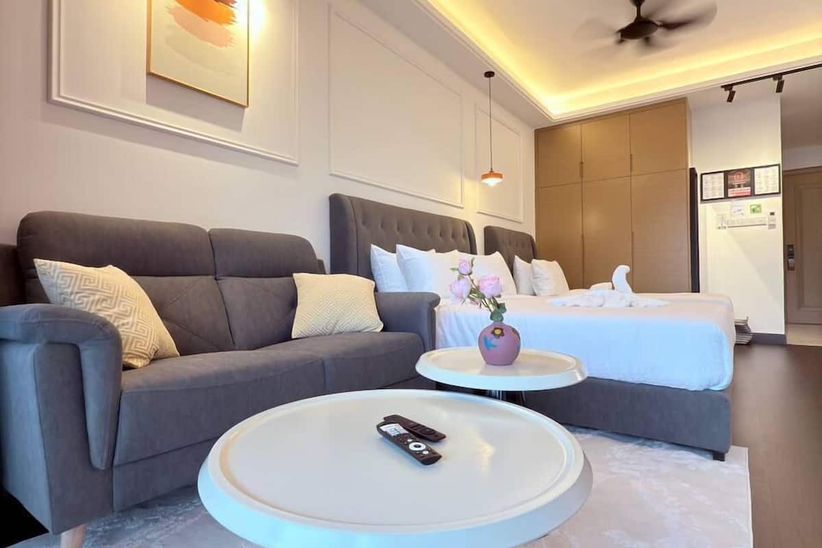 A modern hotel room with a grey sofa, a round coffee table, a bed with white linens, and a ceiling fan.