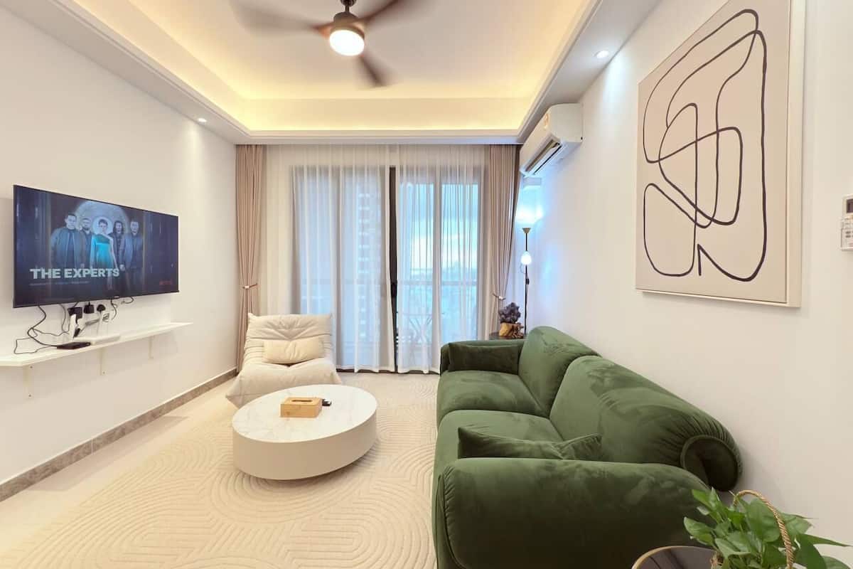 A modern living room with a flat-screen TV, a round coffee table, a green sofa, and a large abstract painting.