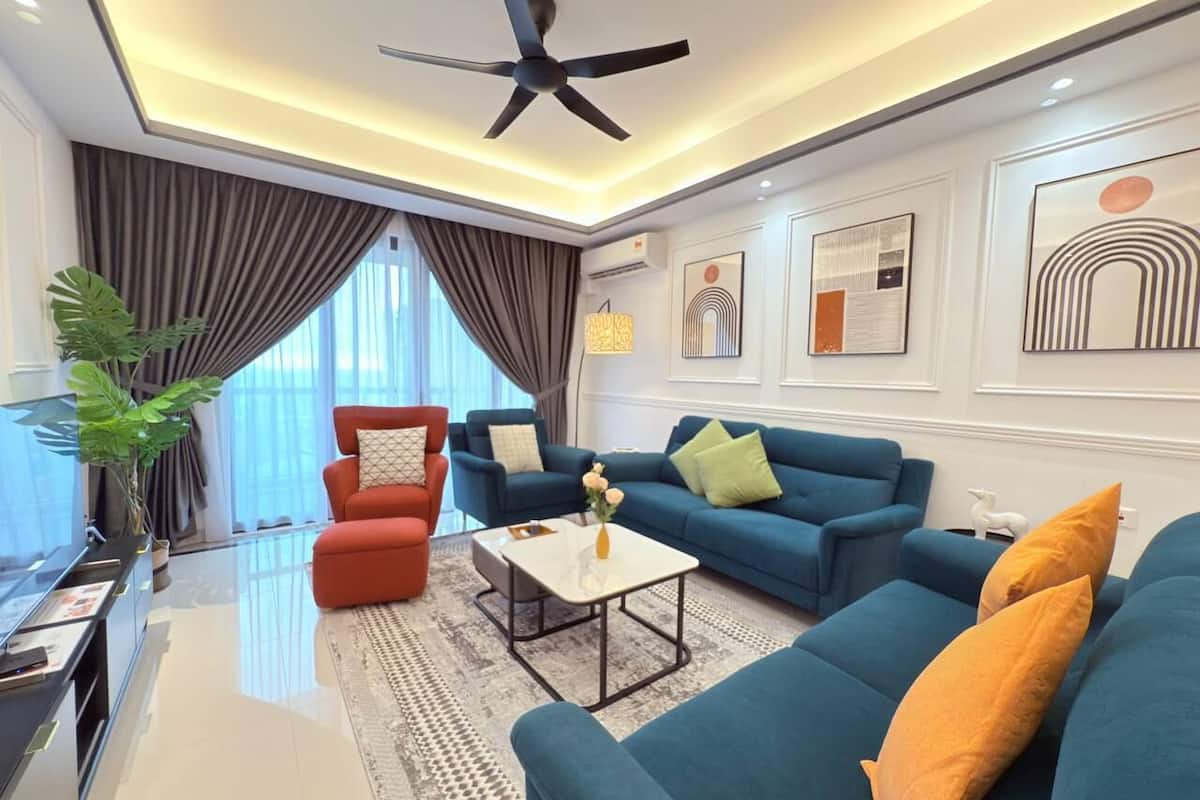 A modern living room with a ceiling fan, a blue sofa set, a red armchair, and a coffee table with a vase of flowers.