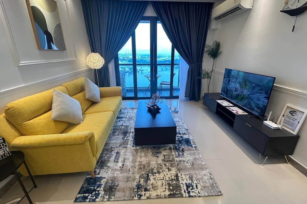A modern living room with a yellow sofa, a coffee table, a flat-screen TV, and a view of the city through large windows.